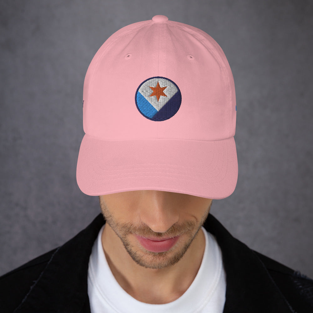 A man facing us wearing a pink Syracuse, NY hat with an embroidered Syracuse city flag design