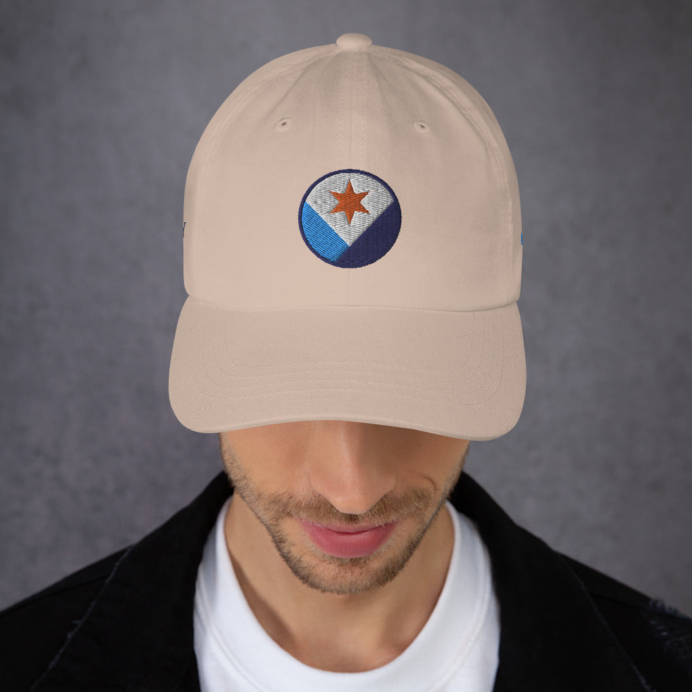 A man facing us wearing a stone colored Syracuse, NY hat with an embroidered Syracuse city flag design