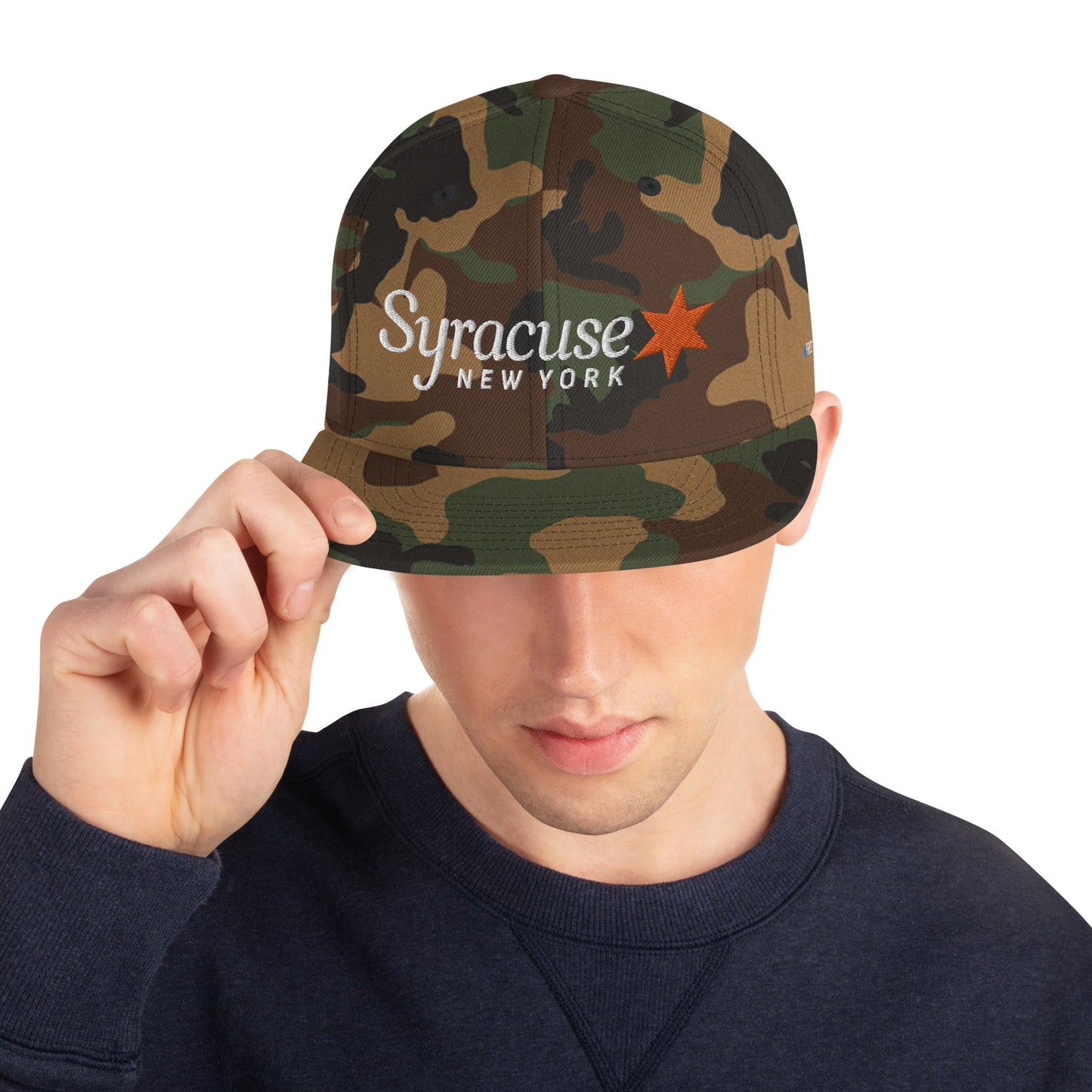 A man facing us wearing a green camouflage Syracuse, NY city flag hat with an embroidered Syracuse, NY logo