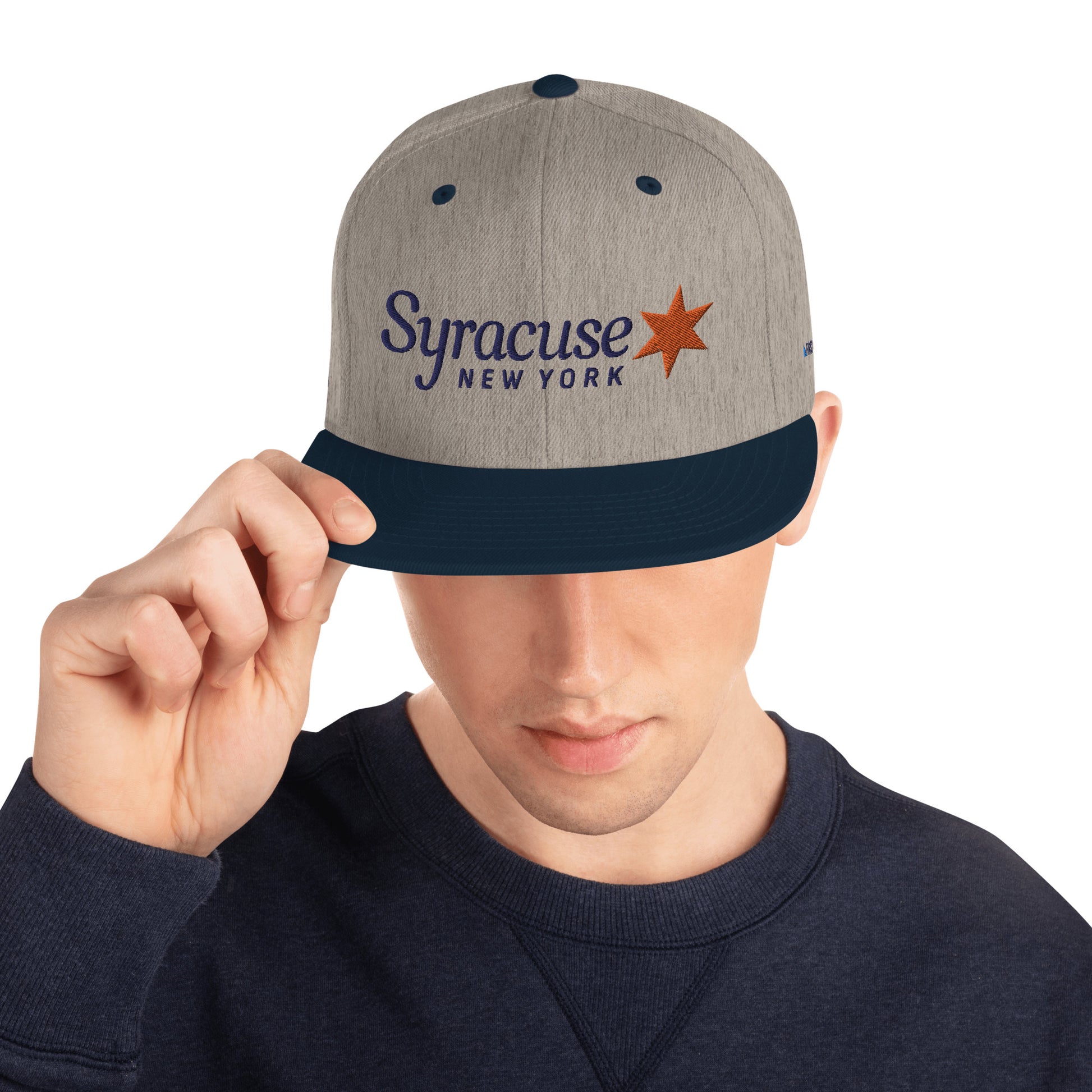 A man facing us wearing a heather grey and navy blue Syracuse, NY city flag hat with an embroidered Syracuse, NY logo