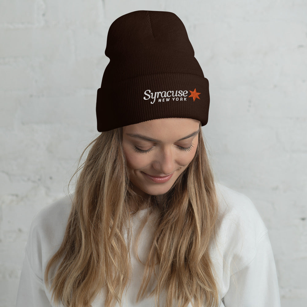 A young woman facing us wearing a brown winter beanie hat embroidered with a Syracuse, NY logo