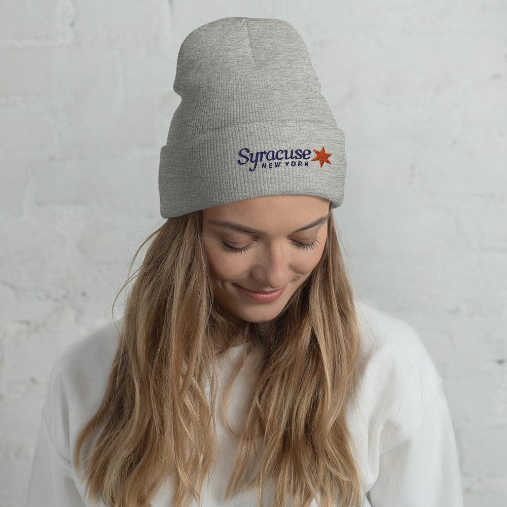 A young woman facing us wearing a heather grey winter beanie hat embroidered with a Syracuse, NY logo