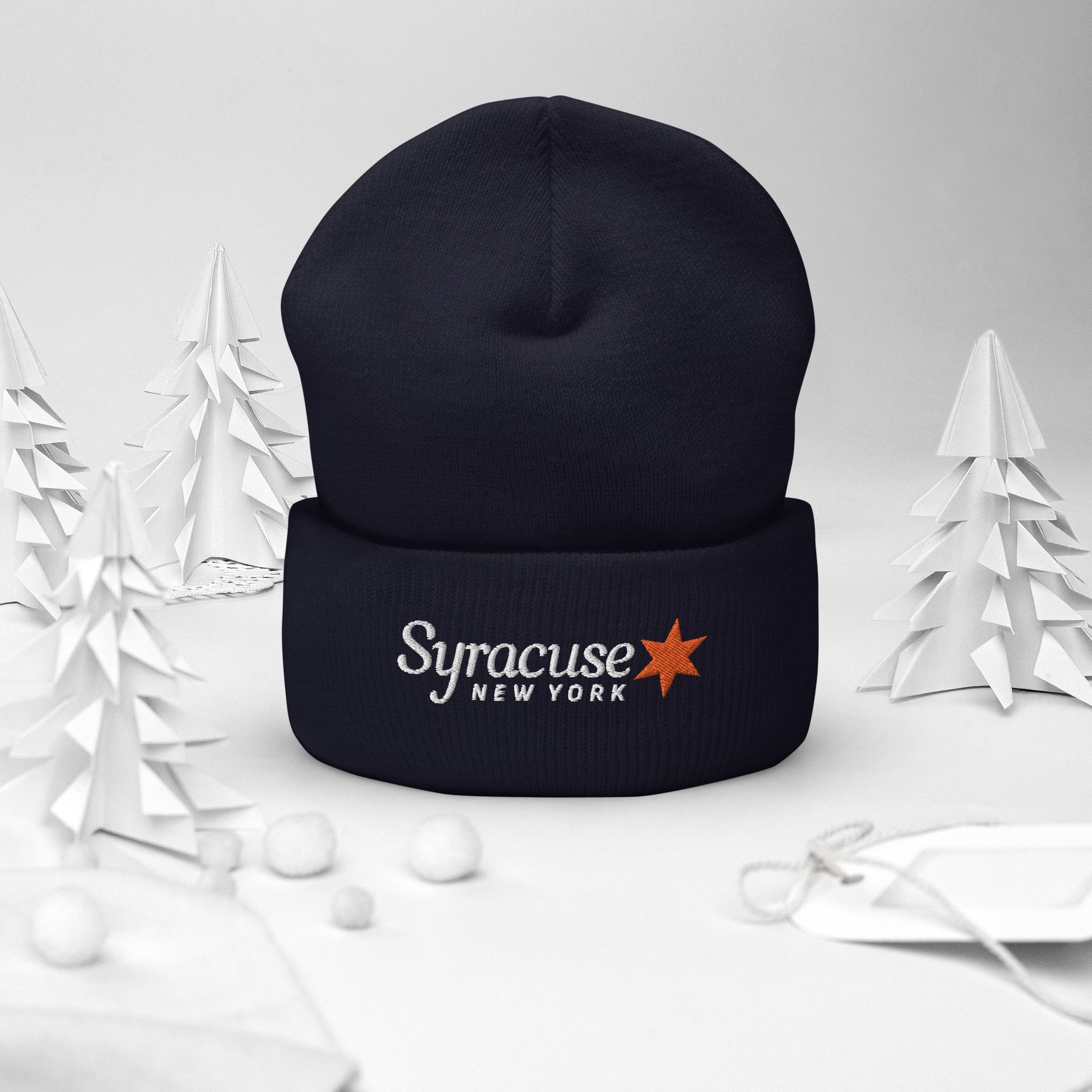 A navy blue Syracuse, NY winter beanie hat embroidered with a Syracuse, NY logo standing upright on a decorative holiday background
