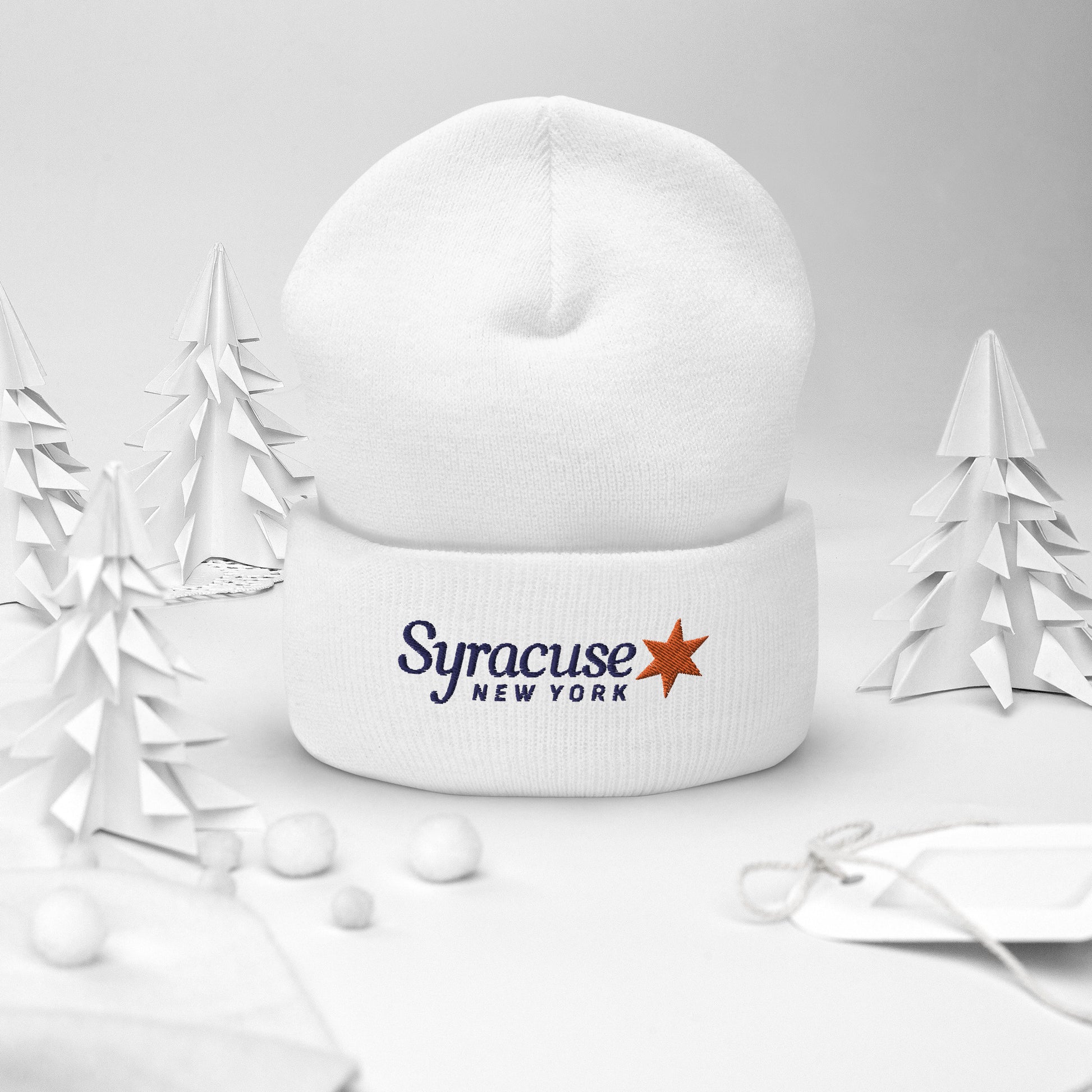 A white Syracuse, NY winter beanie hat embroidered with a Syracuse, NY logo standing upright on a decorative holiday background