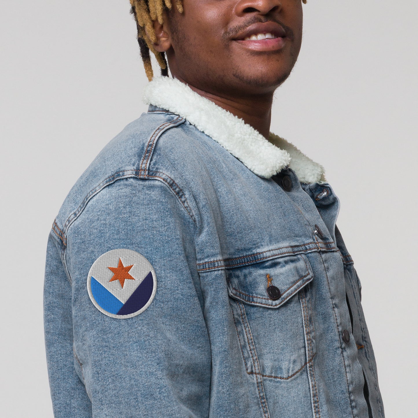 A man wearing a denim jacket with a Syracuse, NY city flag embroidered patch affixed to the sleeve