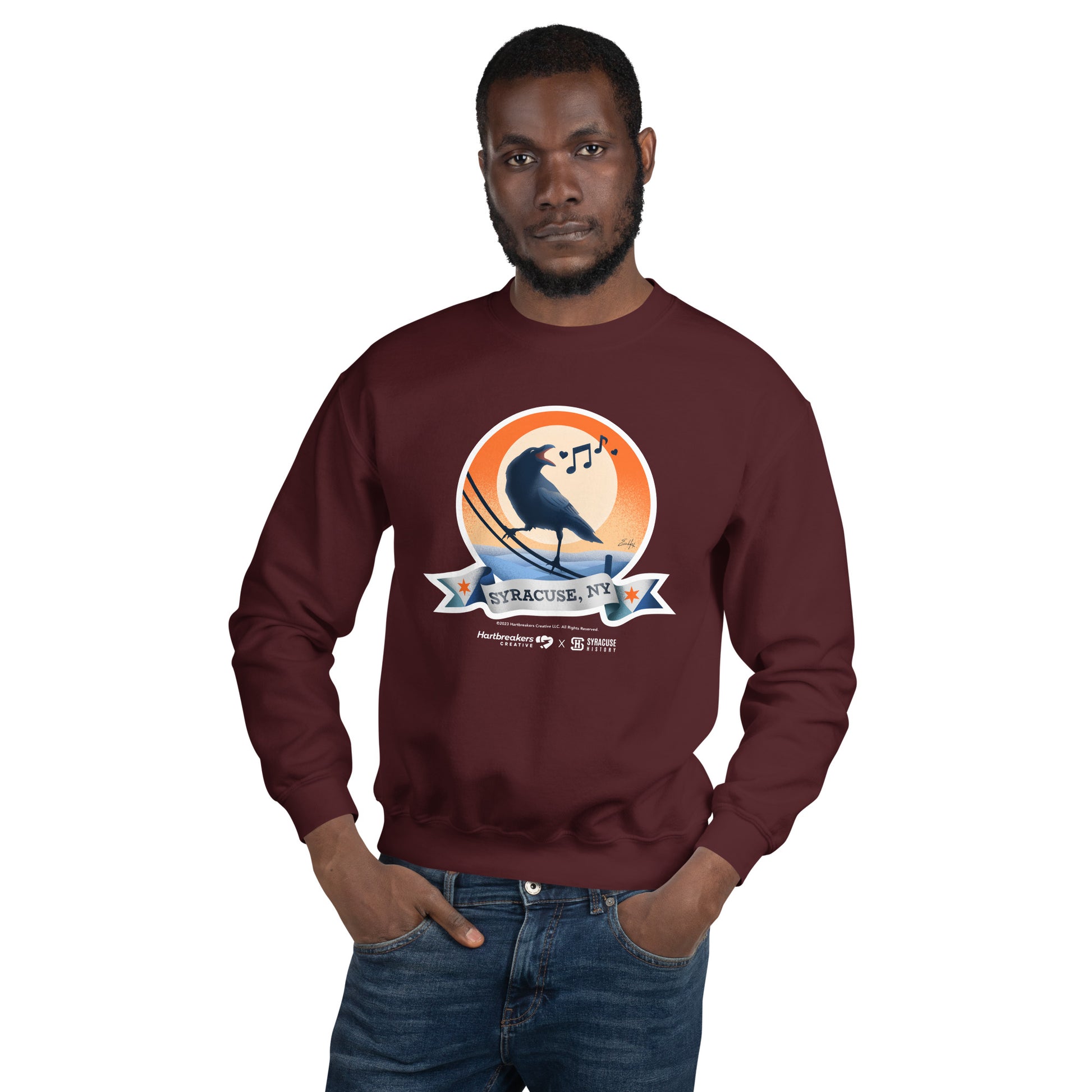 A man wearing a maroon sweatshirt featuring an illustration of a crow on a telephone wire and a banner beneath it that says Syracuse, NY