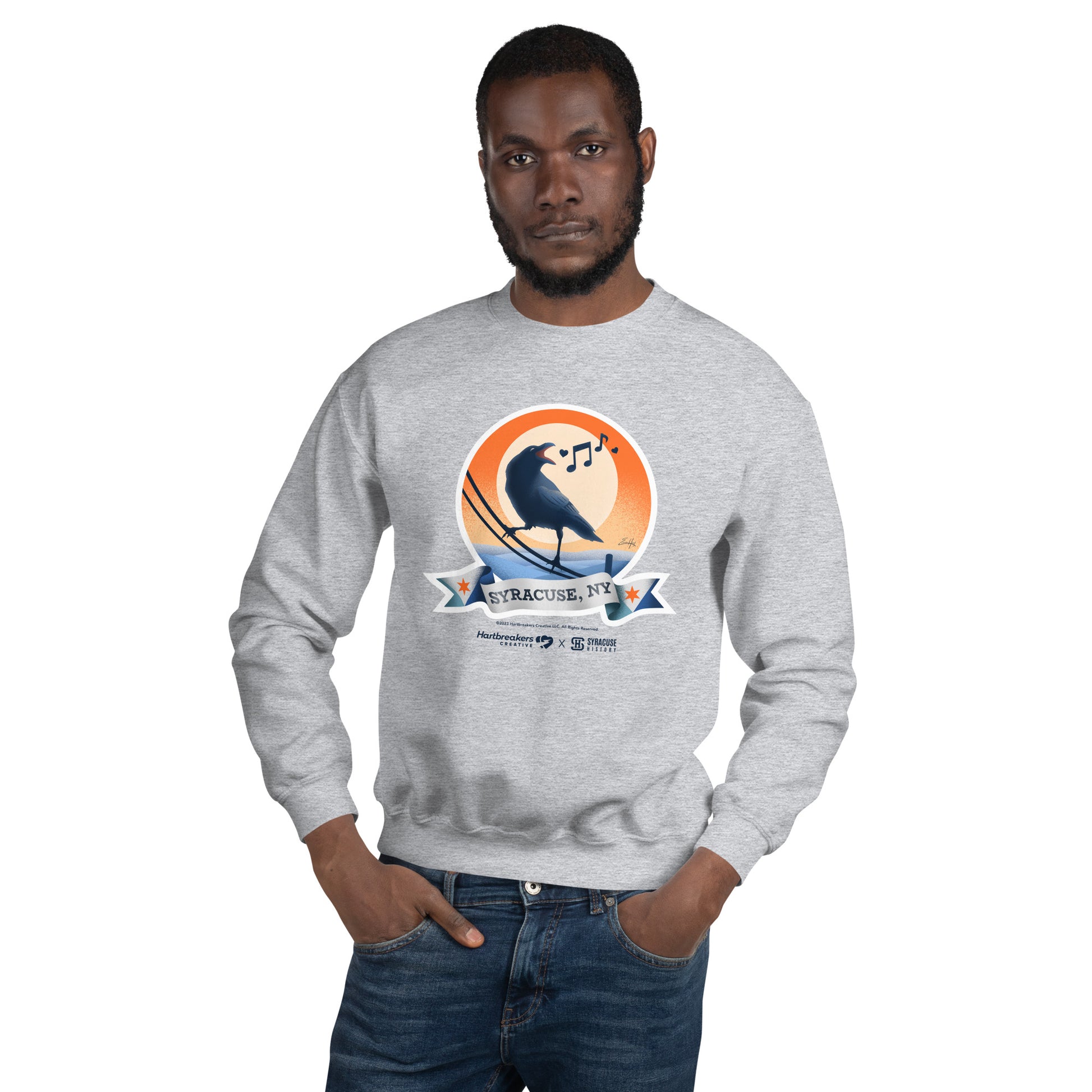 A man wearing a sport grey sweatshirt featuring an illustration of a crow on a telephone wire and a banner beneath it that says Syracuse, NY