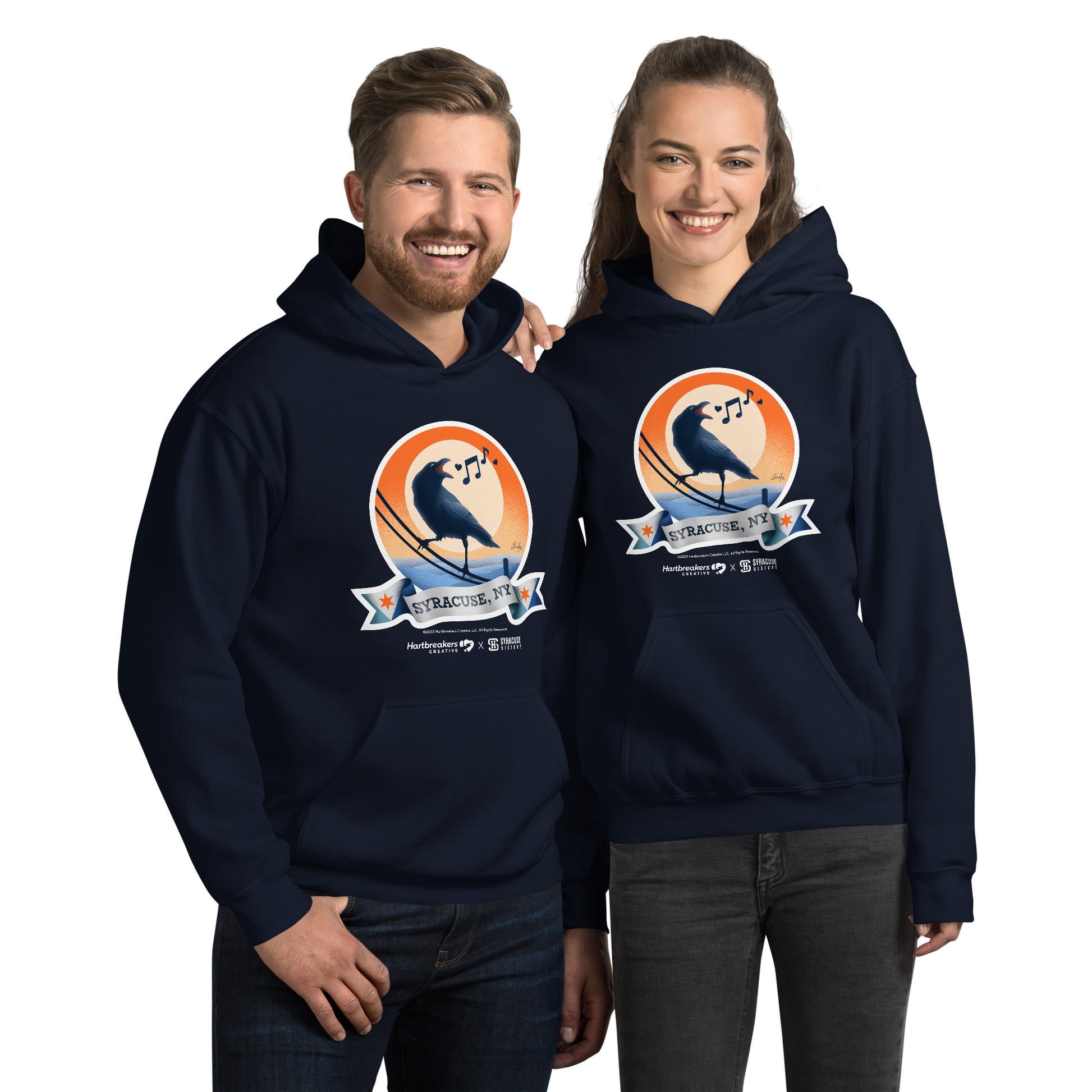 A man and woman wearing navy hoodies featuring an illustration of a crow on a telephone wire and a banner beneath it that says Syracuse, NY