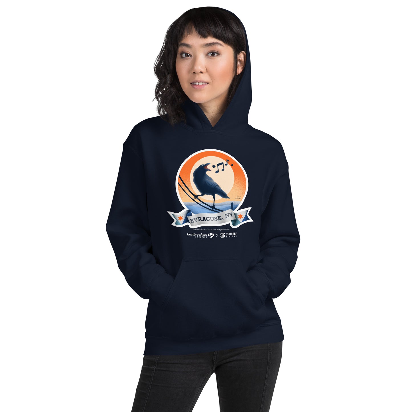 A woman wearing a navy hoodie featuring an illustration of a crow on a telephone wire and a banner beneath it that says Syracuse, NY