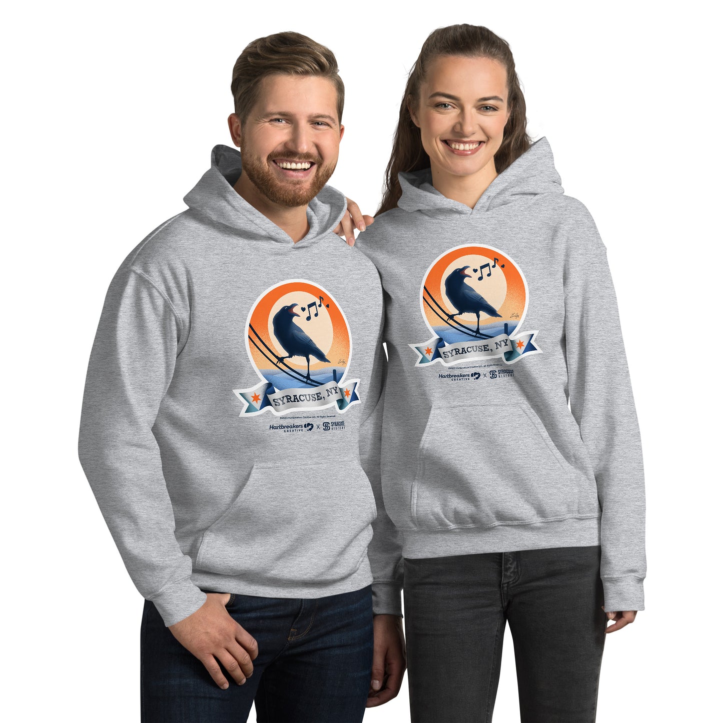 A man and woman wearing sport grey hoodies featuring an illustration of a crow on a telephone wire and a banner beneath it that says Syracuse, NY