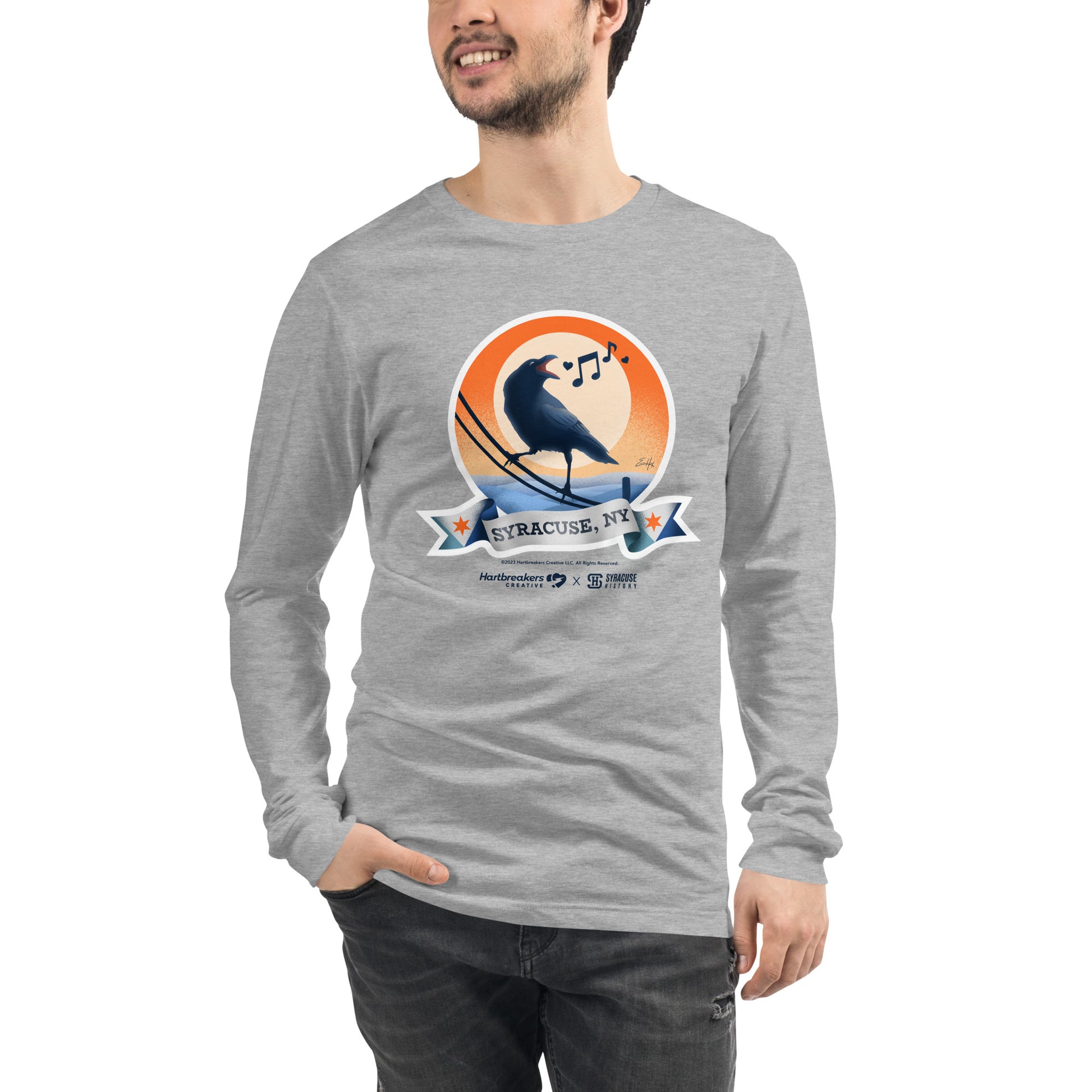 A man wearing an athletic heather long sleeve T-shirt featuring an illustration of a crow on a telephone wire and a banner beneath it that says Syracuse, NY