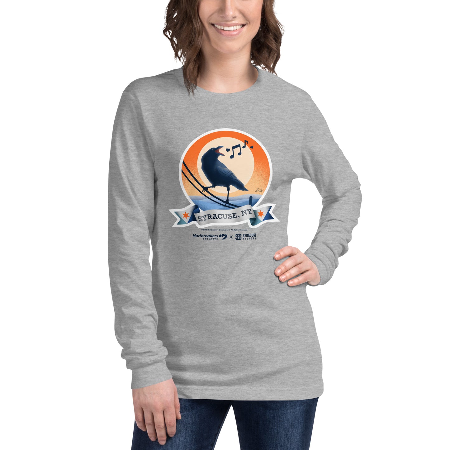 A woman wearing an athletic heather long sleeve T-shirt featuring an illustration of a crow on a telephone wire and a banner beneath it that says Syracuse, NY