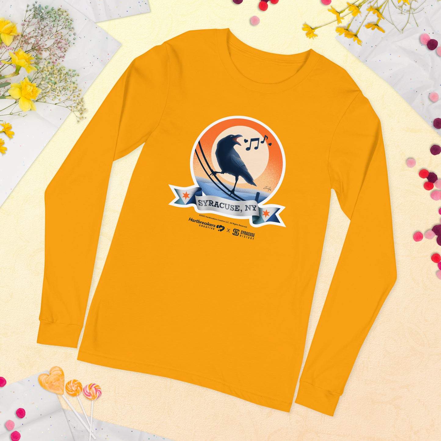 A gold-colored long sleeve T-shirt featuring an illustration of a crow on a telephone wire and a banner beneath it that says Syracuse, NY