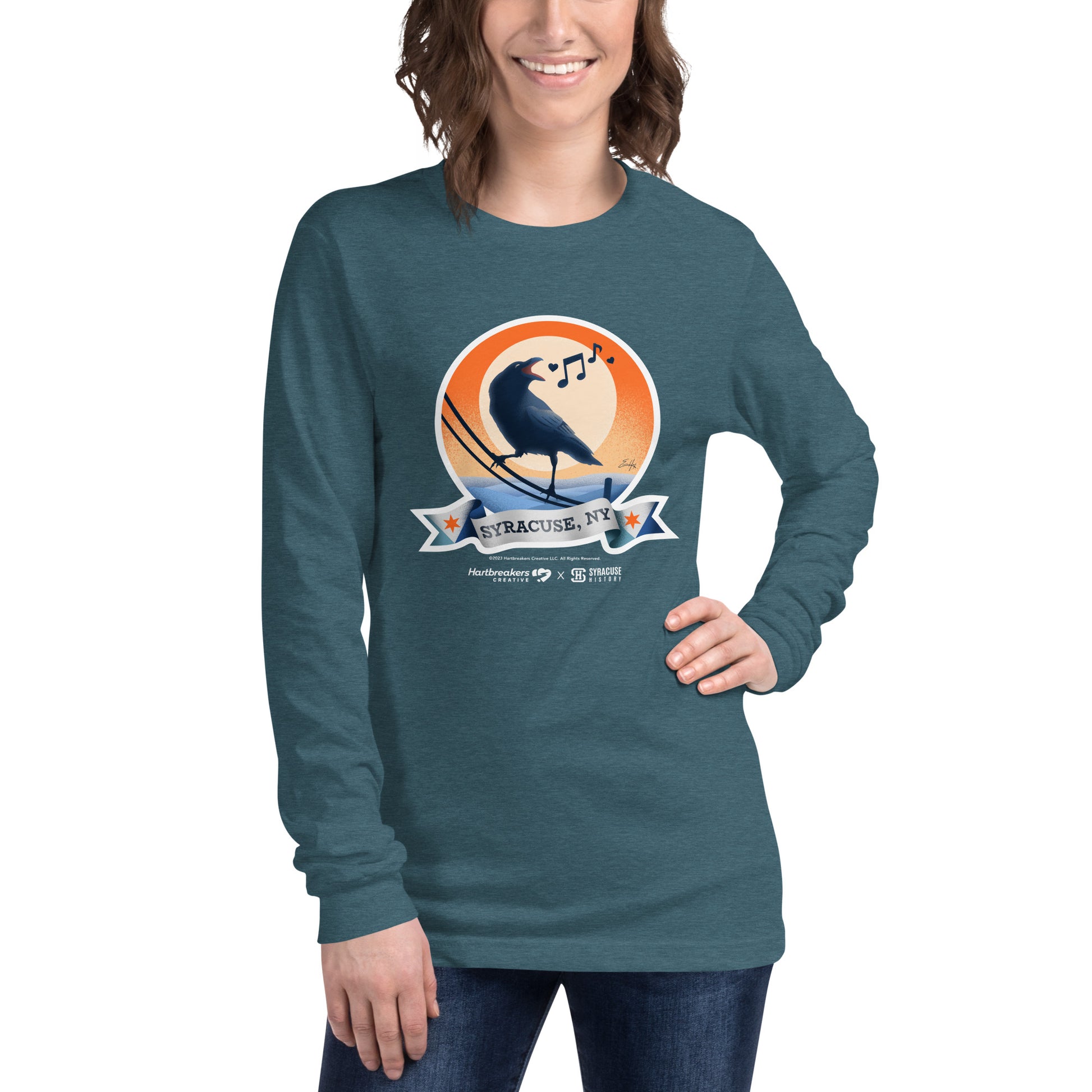A woman wearing a heather teal long sleeve T-shirt featuring an illustration of a crow on a telephone wire and a banner beneath it that says Syracuse, NY