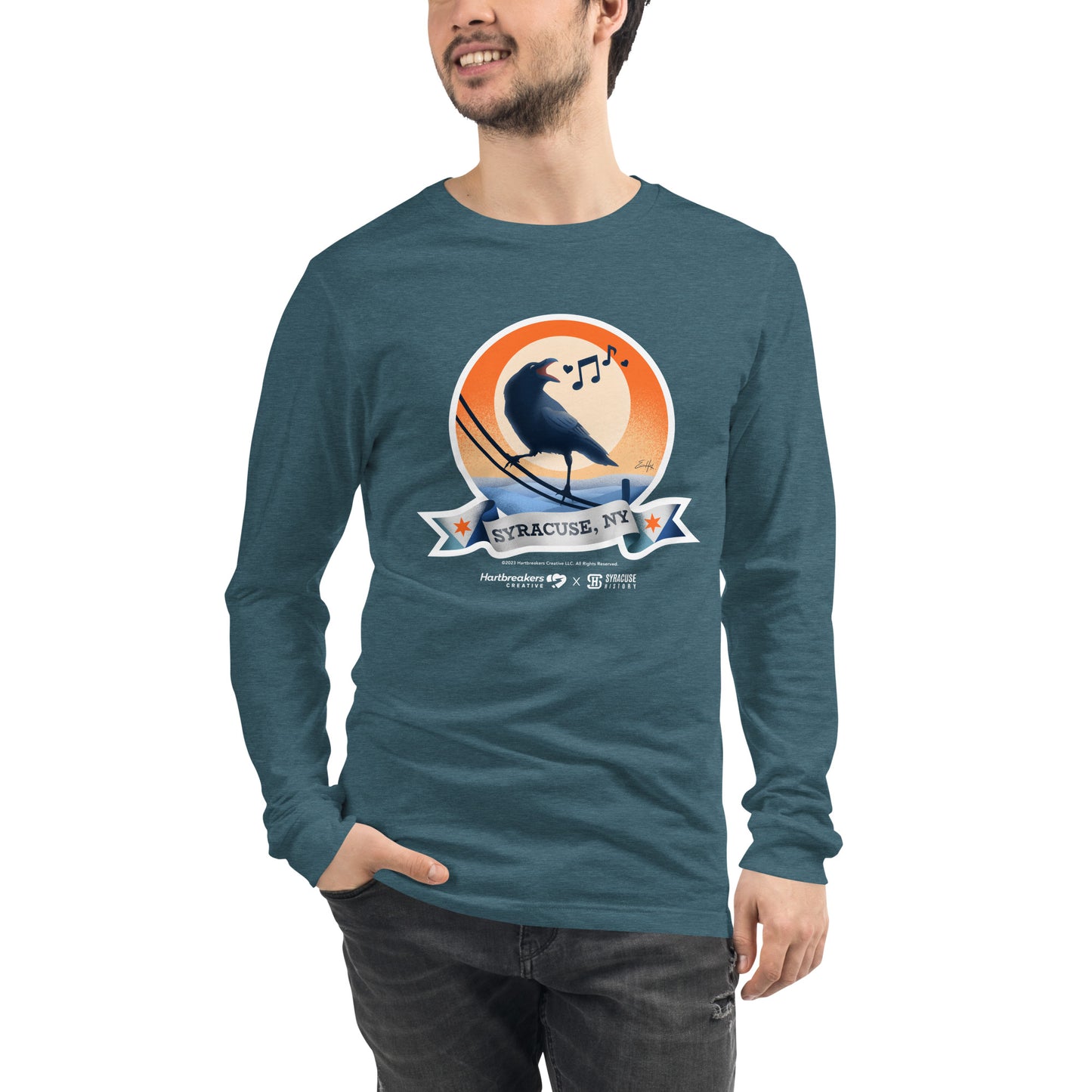 A man wearing a heather teal long sleeve T-shirt featuring an illustration of a crow on a telephone wire and a banner beneath it that says Syracuse, NY