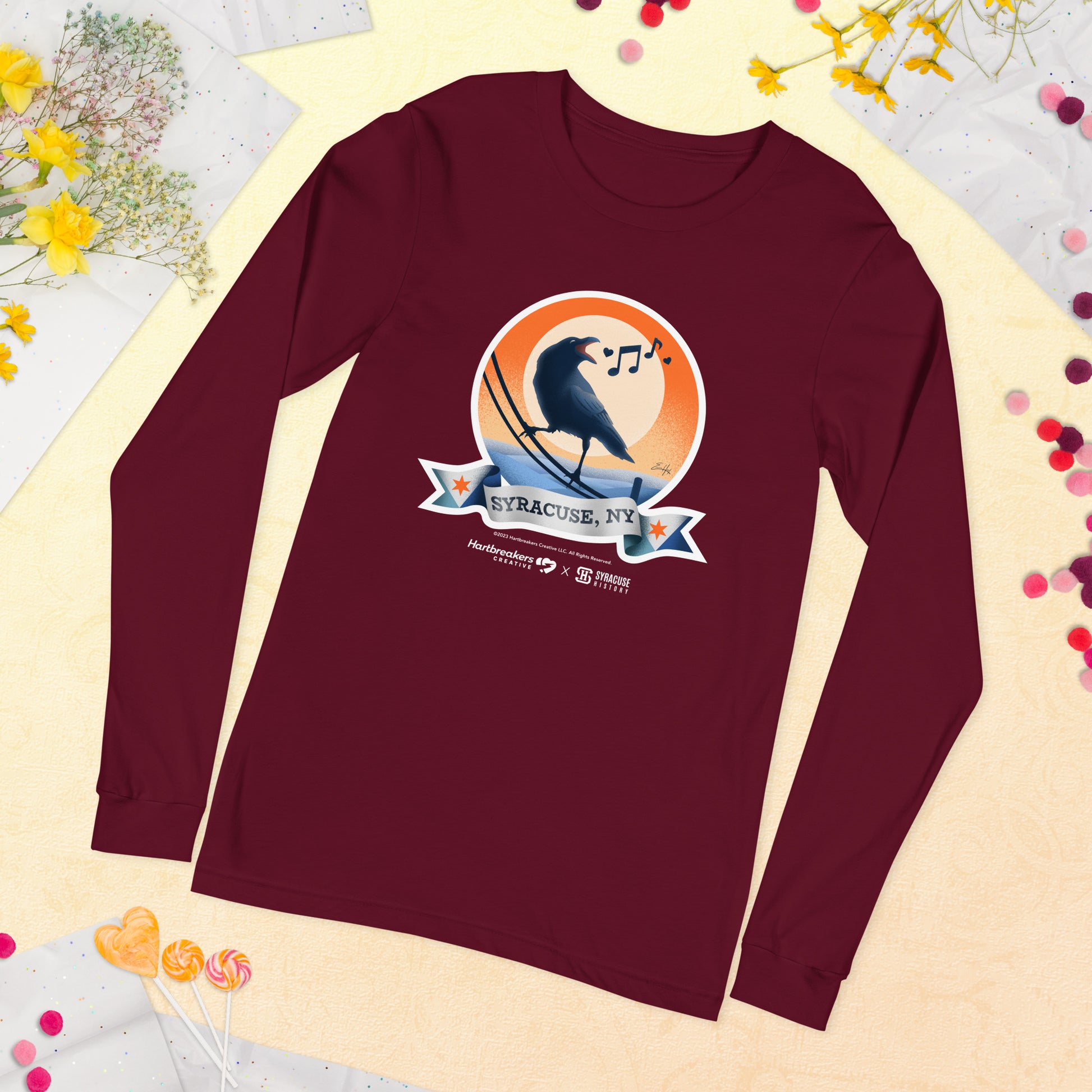 A maroon long sleeve T-shirt featuring an illustration of a crow on a telephone wire and a banner beneath it that says Syracuse, NY