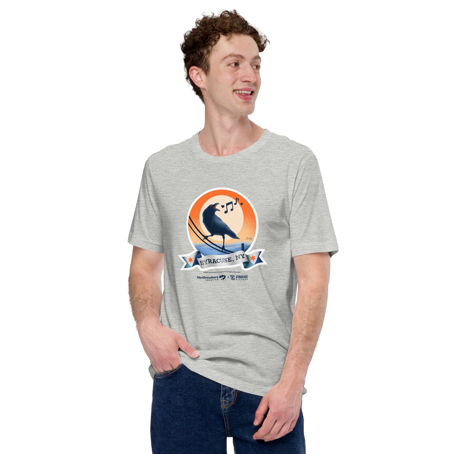 A man wearing an athletic heather T-shirt featuring an illustration of a crow on a telephone wire and a banner beneath it that says Syracuse, NY