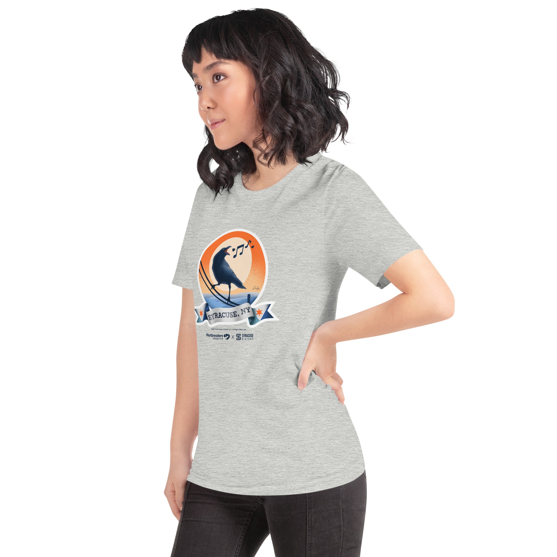 A woman wearing an athletic heather T-shirt featuring an illustration of a crow on a telephone wire and a banner beneath it that says Syracuse, NY