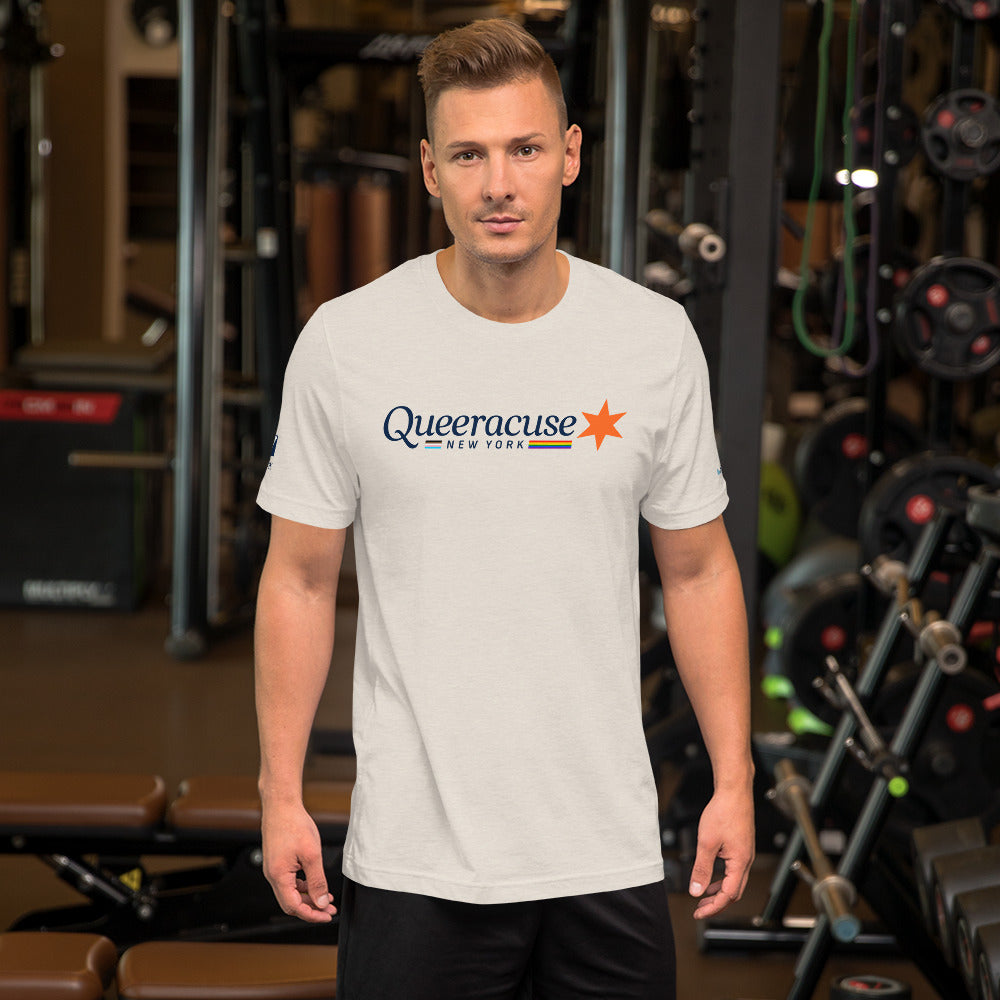A man in a gym facing us wearing a heather dust colored Syracuse, NY t-shirt featuring a Queeracuse logo
