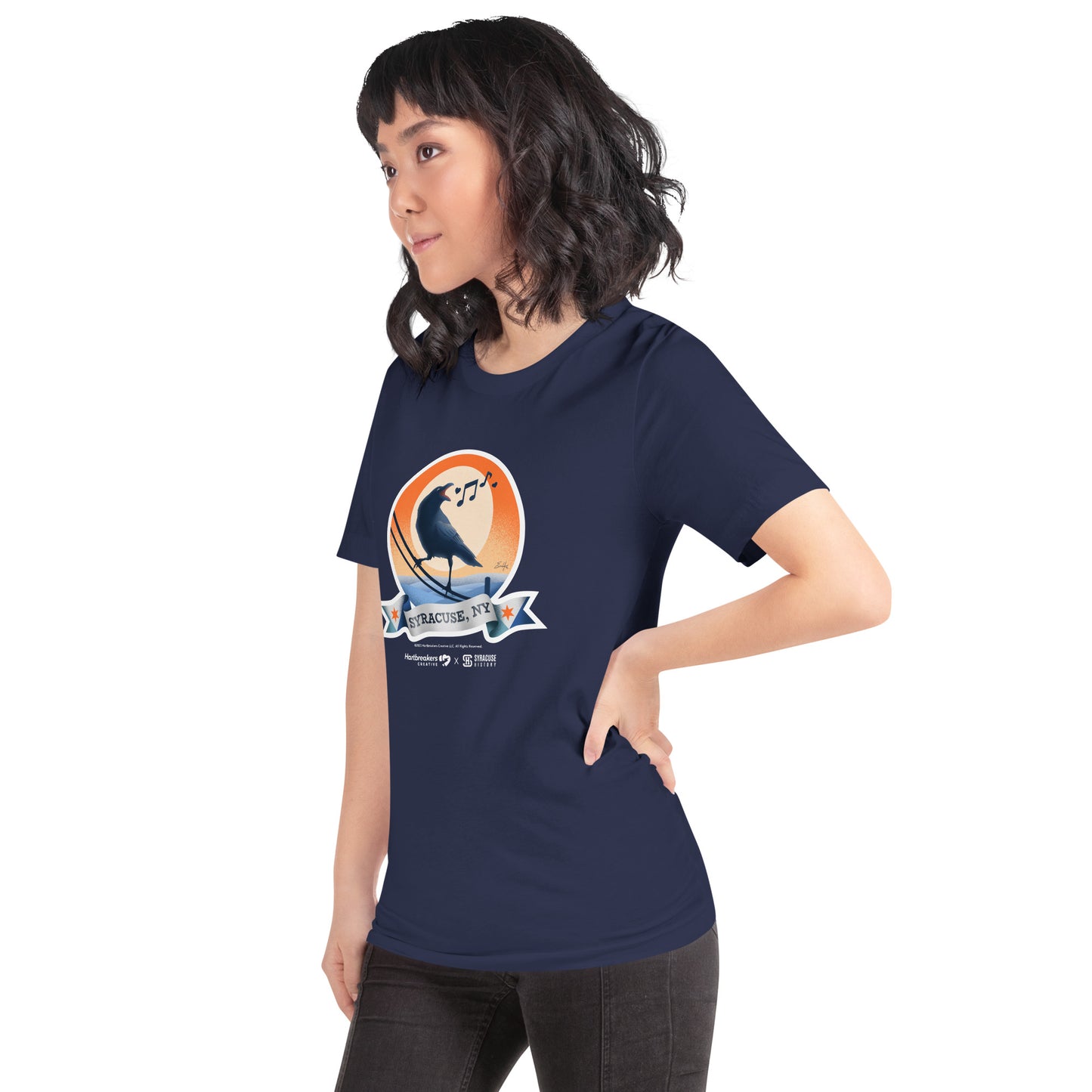 A woman wearing a navy T-shirt featuring an illustration of a crow on a telephone wire and a banner beneath it that says Syracuse, NY